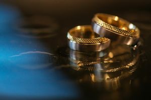 Close-up of two textured gold wedding rings on reflective blue surface.