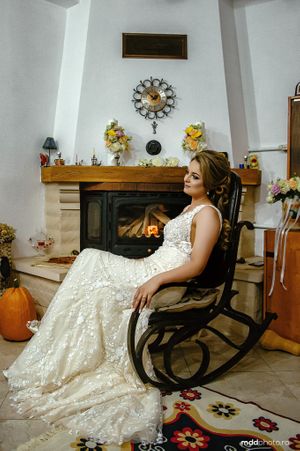Elegant lace wedding dress displayed in a cozy autumn setting with fireplace and pumpkin decor.