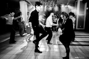 Energetic black and white photo of guests dancing at a wedding reception.