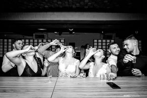 Black and white photo of wedding party taking shots together at a bar counter.