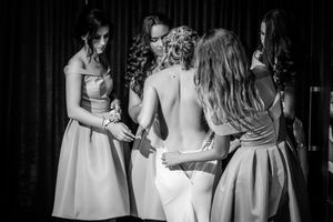 Black and white candid shot of bridesmaids helping with wedding dress preparations.