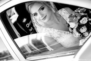 Black and white portrait of bride with bouquet sitting in wedding car.