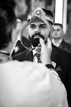 A bearded man wearing a decorative crown and suit during a traditional Orthodox wedding ceremony.