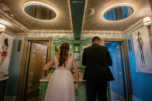 Couple in wedding attire viewed from behind in elegant hallway with circular ceiling lights.