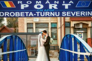 Newlyweds share a romantic moment on a blue bridge in front of a Romanian train station.