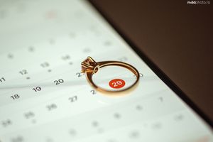 A gold engagement ring sits on a calendar marking an important date.