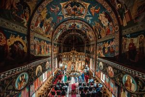 An Orthodox church ceremony captured from above showing ornate painted ceiling and gathered congregation.