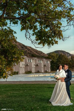 A romantic wedding portrait captured under tree branches with mountains in background.