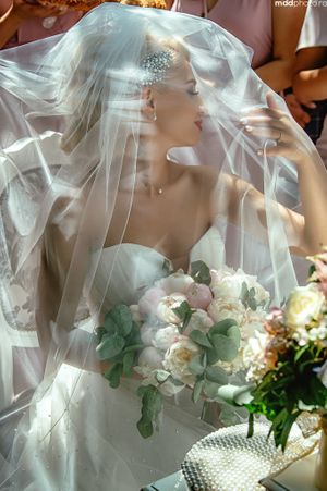 A bridal portrait showing a delicate veil and white bouquet with eucalyptus accents in soft lighting.