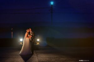 A romantic nighttime wedding portrait with car headlights and street lamp creating dramatic lighting.