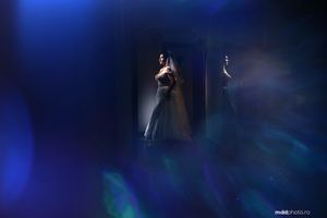 A silhouetted figure in an evening gown stands against dramatic blue stage lighting.