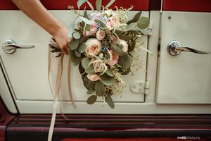 An elegant bridal bouquet with blush roses and eucalyptus leaves held against white doors.