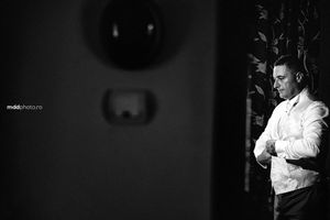 A black and white portrait of a person in formal attire standing in dramatic lighting.