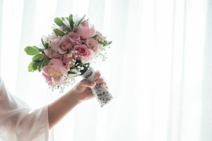 Delicate pink rose bridal bouquet held against soft white curtain background.
