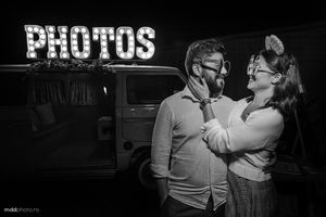 Black and white nighttime portrait in front of illuminated 'PHOTOS' sign.