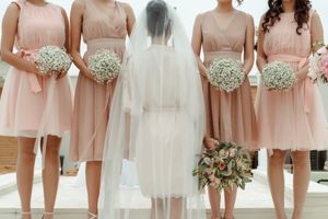 Bridesmaids in blush pink dresses holding white bouquets standing with bride in veil.