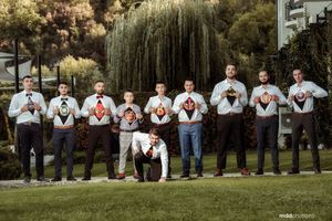 Groomsmen in matching outfits display superhero shirts under their dress clothes in a garden setting.