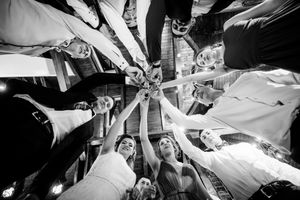 Black and white overhead shot of people raising drinks in a celebratory circle.