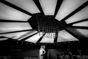 Black and white wedding reception photograph under a geometric ceiling with chandeliers.