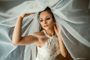 Ethereal bridal portrait with flowing veil against soft white background.