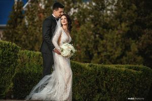Elegant wedding couple embraces by a manicured hedge in an outdoor garden setting.