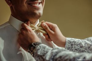 Close-up of hands adjusting a cream bowtie on formal attire.