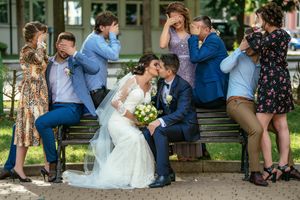 Wedding party gathered on steps striking playful 'see no evil, hear no evil, speak no evil' poses together.