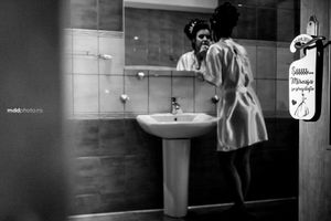 Black and white image of a person looking in bathroom mirror by vintage sink.