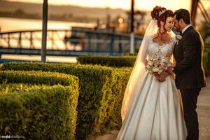 Sunset wedding portrait with couple standing by manicured hedges.