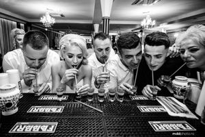 Black and white photo of party guests doing shots at bar.