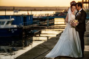 Waterfront wedding portrait at sunset with boats in background.
