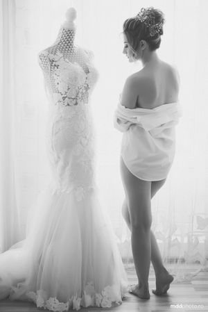Black and white portrait of bride in flowing gown framed by overhanging trees.