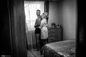 Black and white image of couple embracing in bedroom before wedding ceremony.