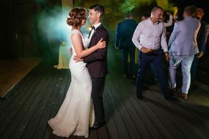 Newlyweds share first dance while guests mingle in background at reception.