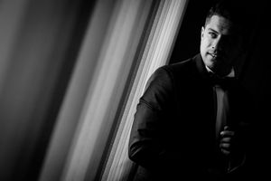 Dramatic side-lit black and white portrait in formal attire near window.