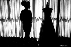 Silhouettes of dress form and figure against backlit curtained window.