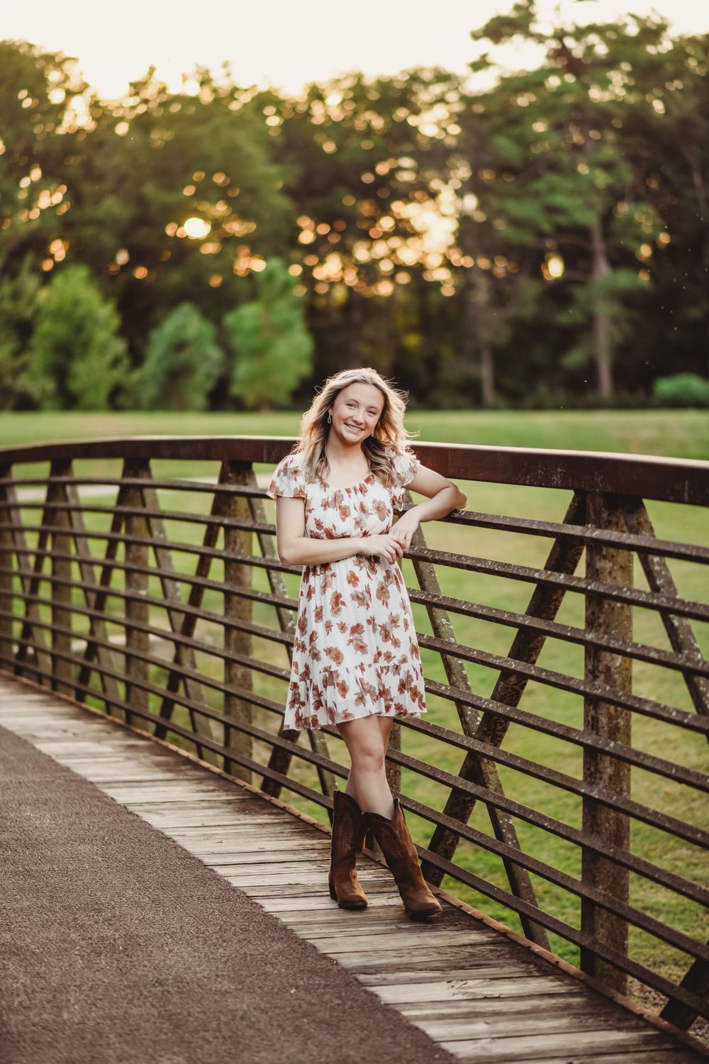 Brown boots and floral dress pose on wooden bridge during sunset in park setting.
