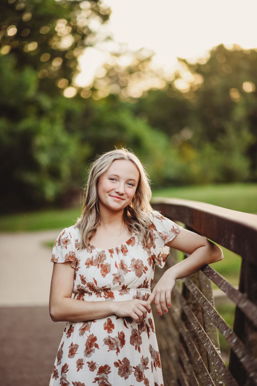 White and brown floral dress stands against rustic wooden bridge railing at golden hour.