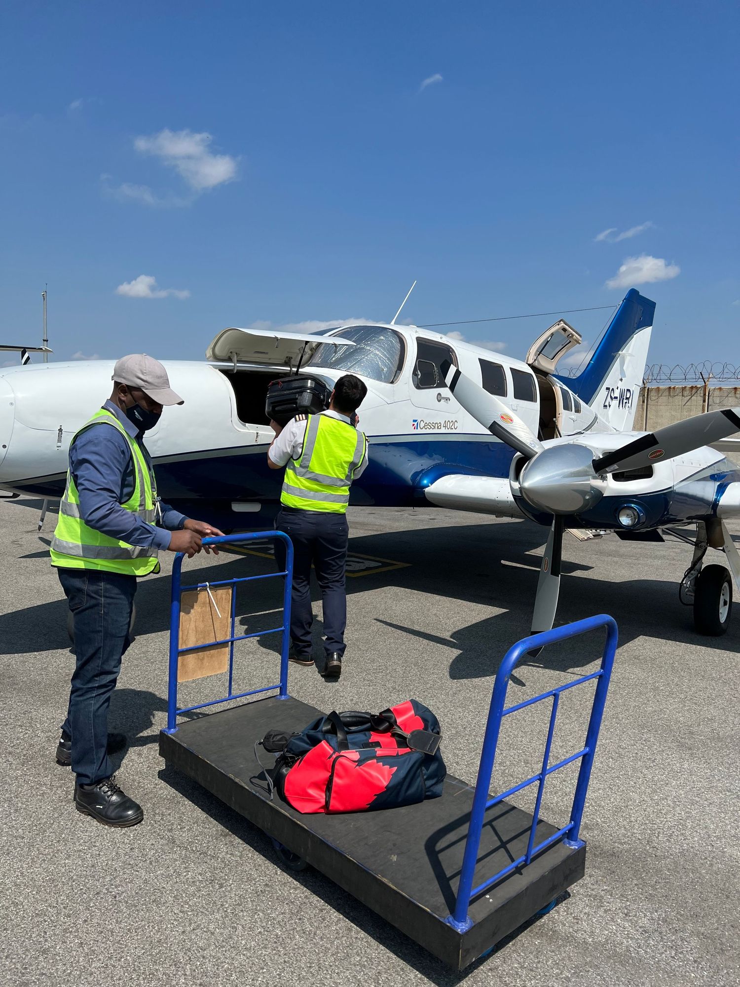 Small aircraft on tarmac with blue loading ramp and luggage being loaded.
