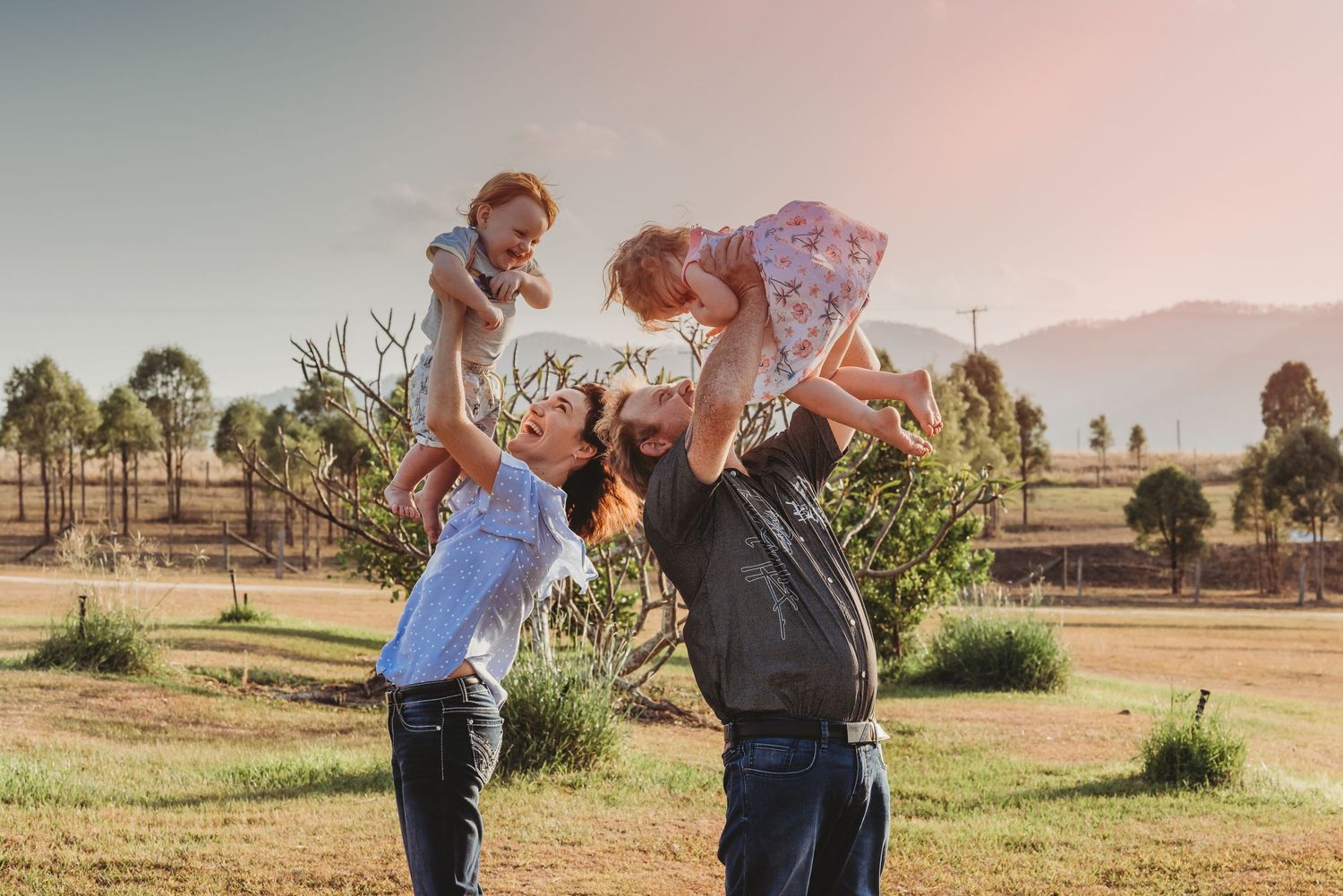 Playful family moment captured in outdoor setting with sunset lighting.