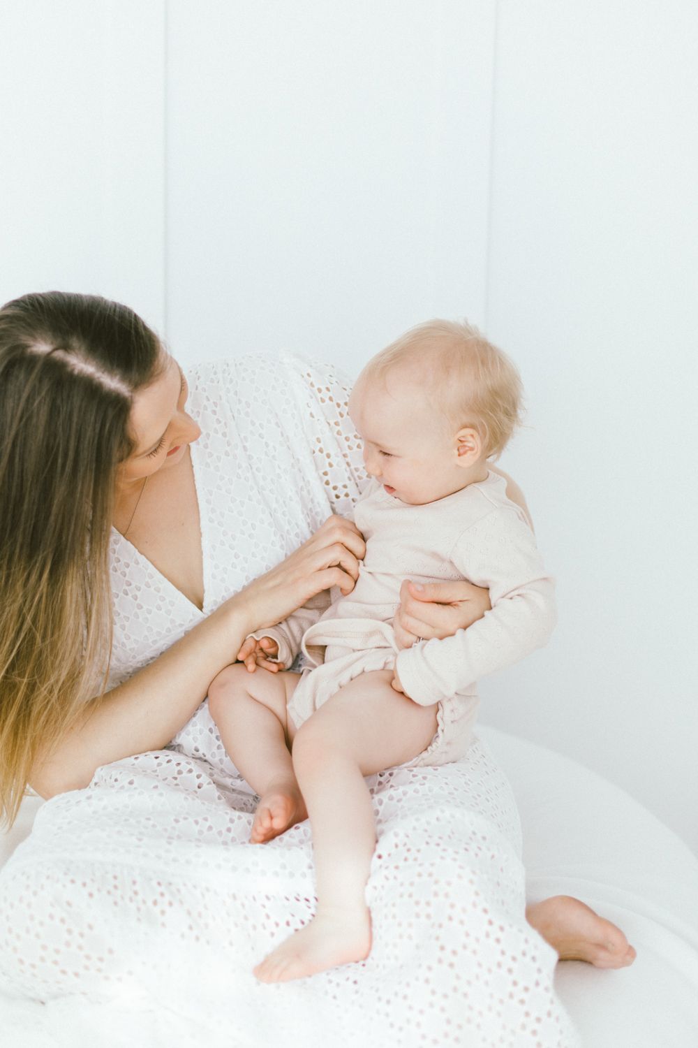 Parent and baby share intimate bonding moment on white bedding.