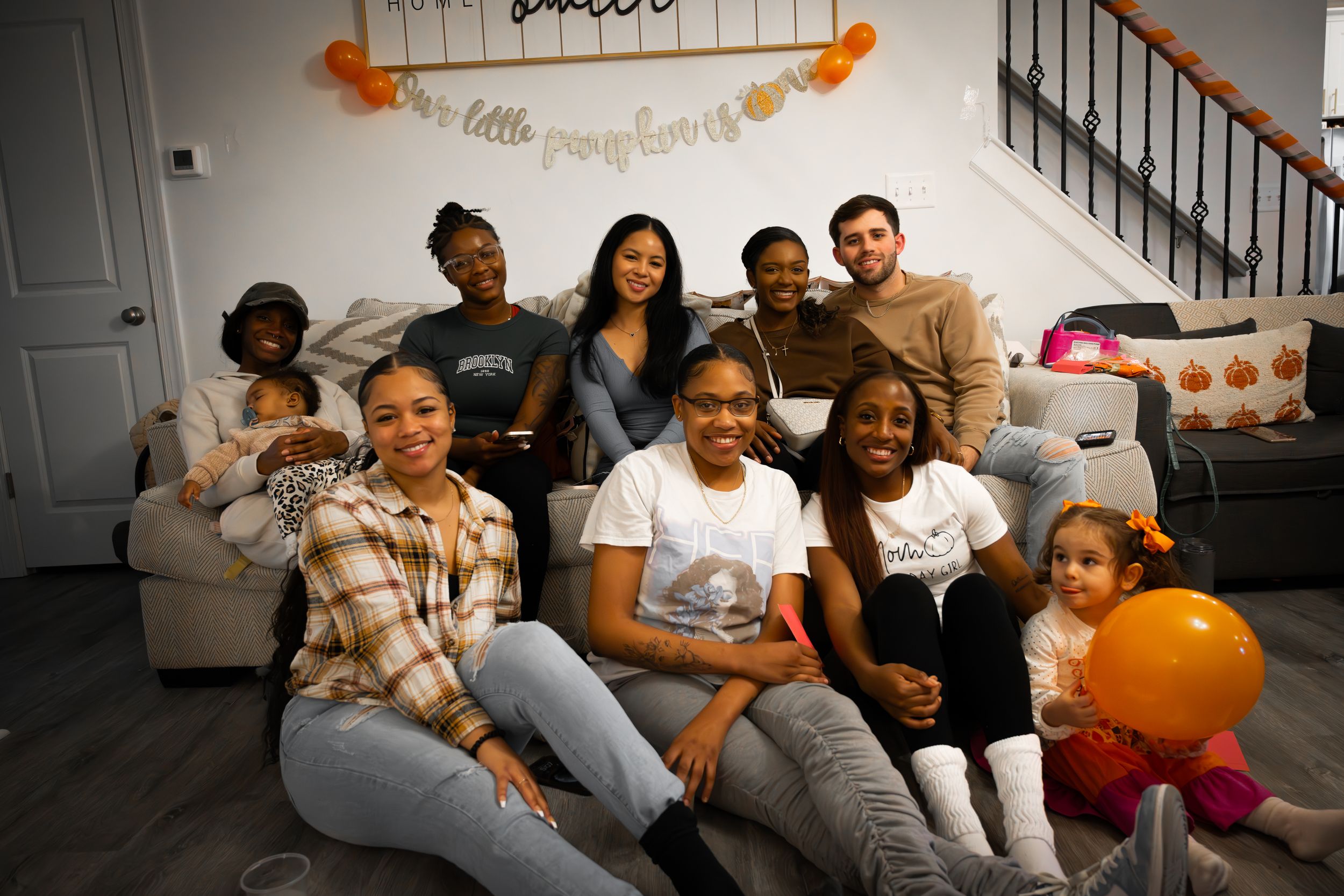 A group poses together on a gray couch during a casual home gathering.