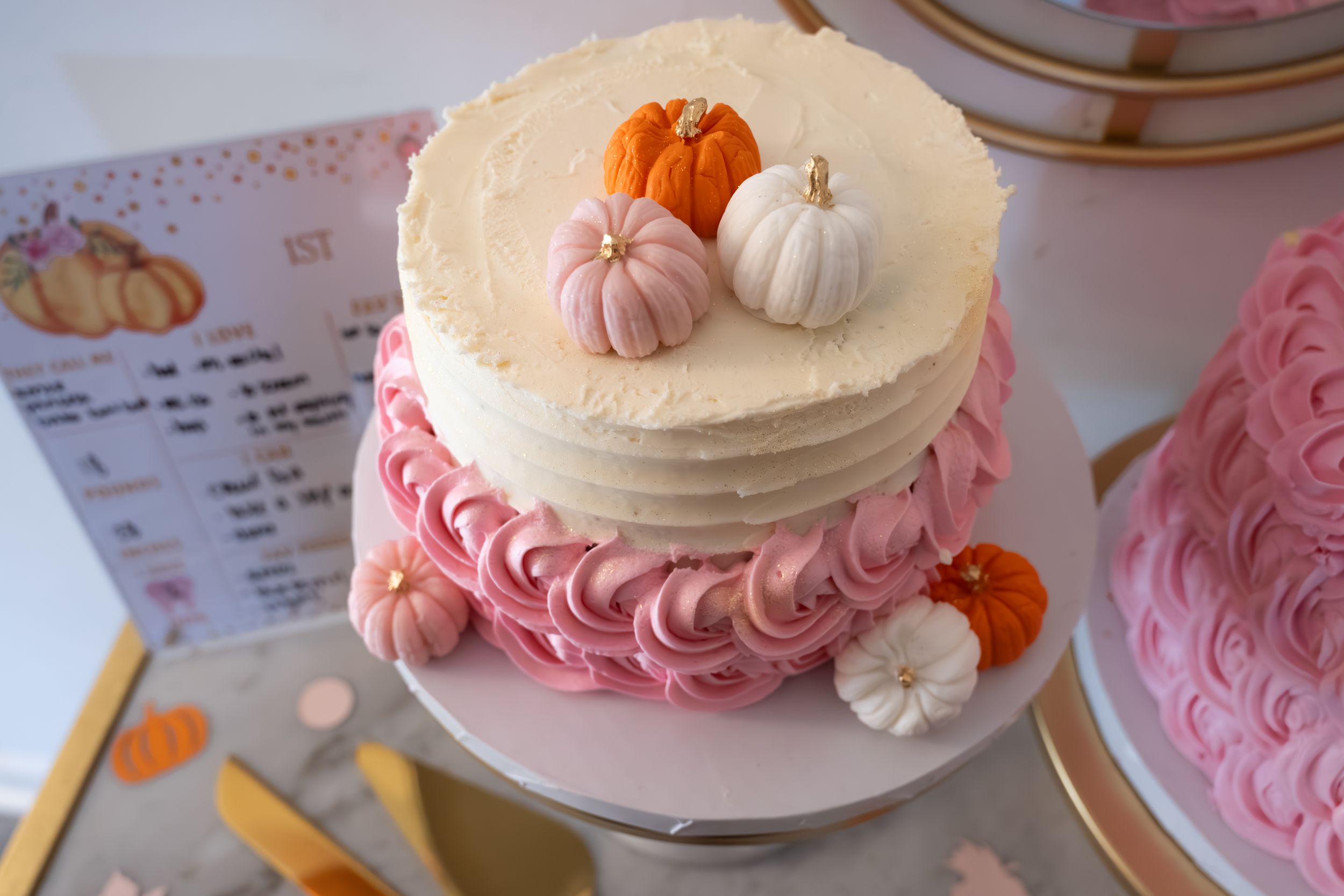 Two-tiered cake with pink rosettes and miniature pumpkin decorations on top.