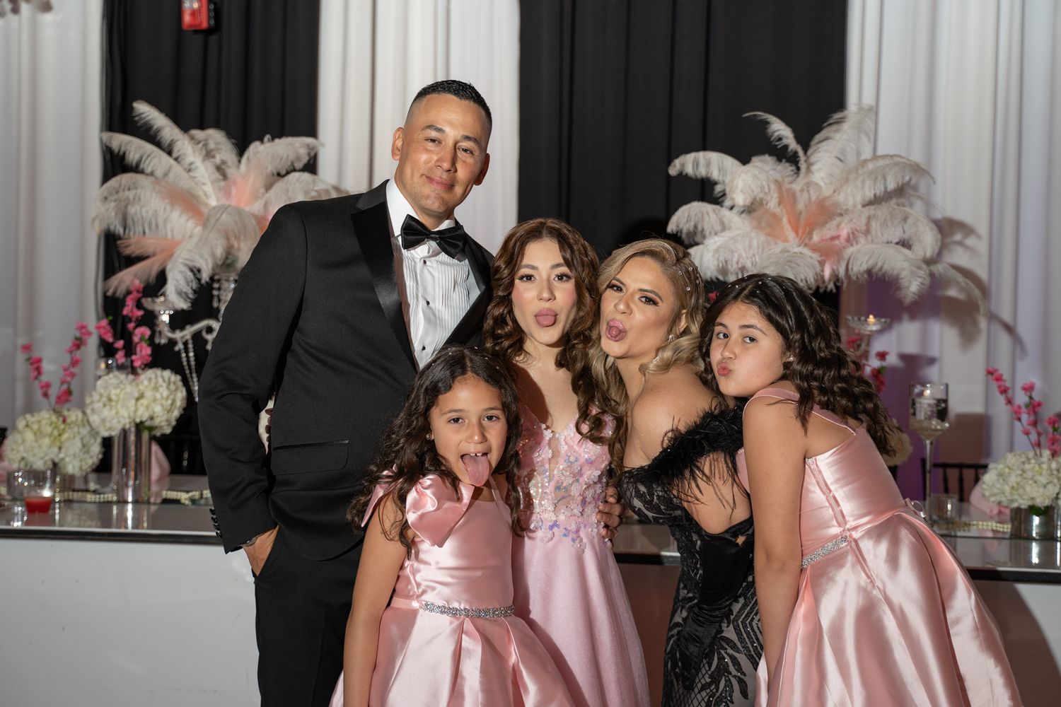 Sweet 15 party in formal attire posing together in an elegant venue with pink and white floral decorations.