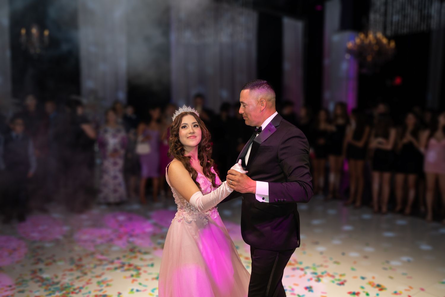 Couple sharing a romantic dance moment under pink lighting with confetti on the dance floor.