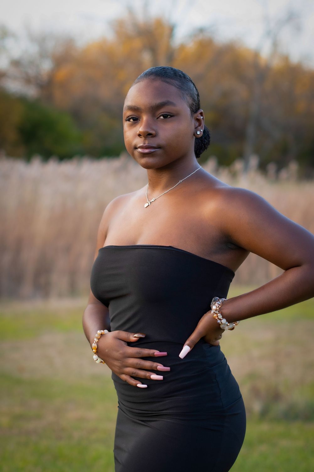 Maternity photoshoot in black dress against natural outdoor setting with golden grass.
