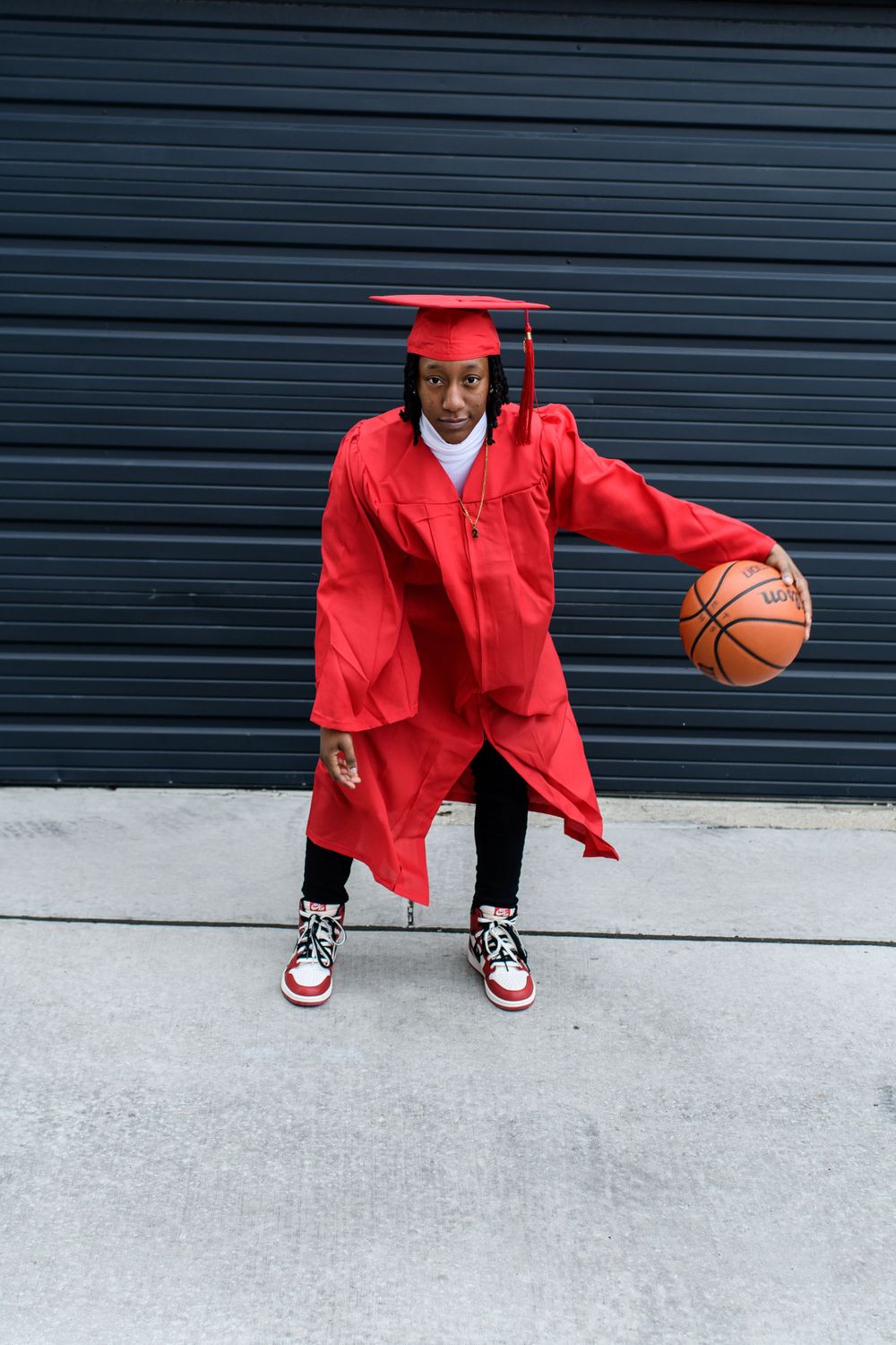 Graduation photo featuring someone dribbling basketball while wearing red cap and gown.