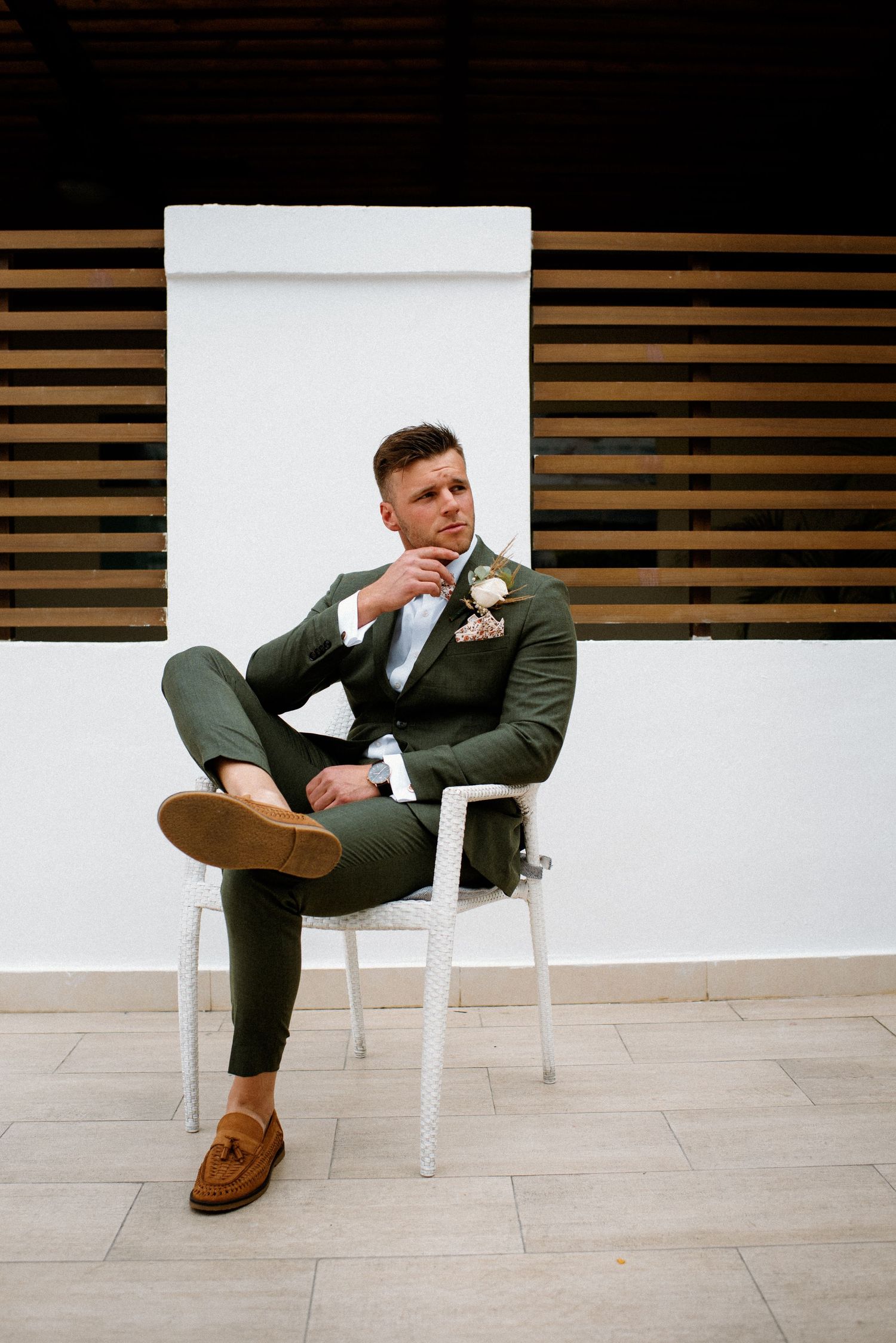 Modern wedding photography with someone posing on white chairs against wooden wall panels.