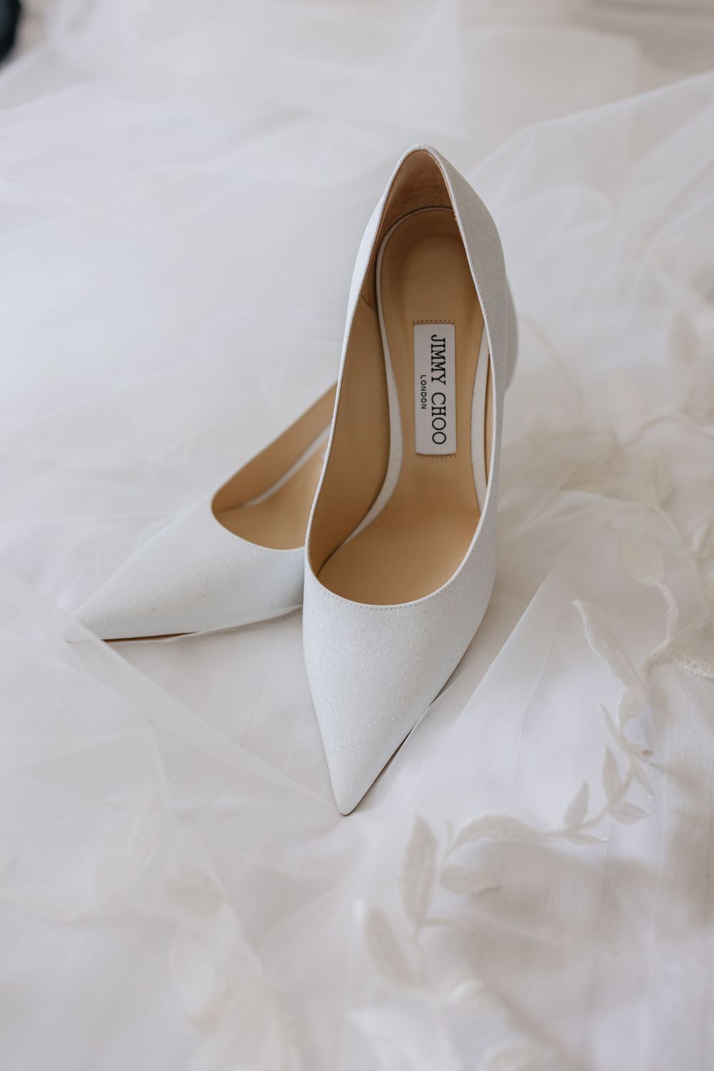 Elegant white Jimmy Choo pointed-toe wedding heels on white fabric background.