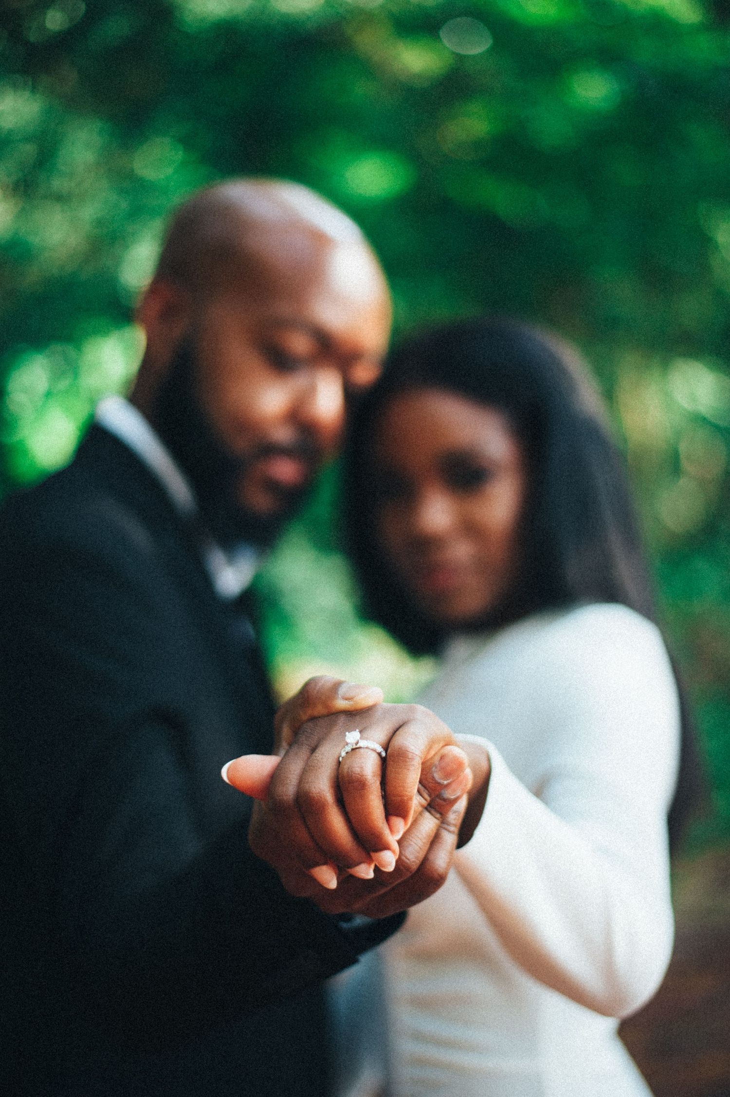 A couple holds hands and shows off their wedding rings in a romantic outdoor setting.